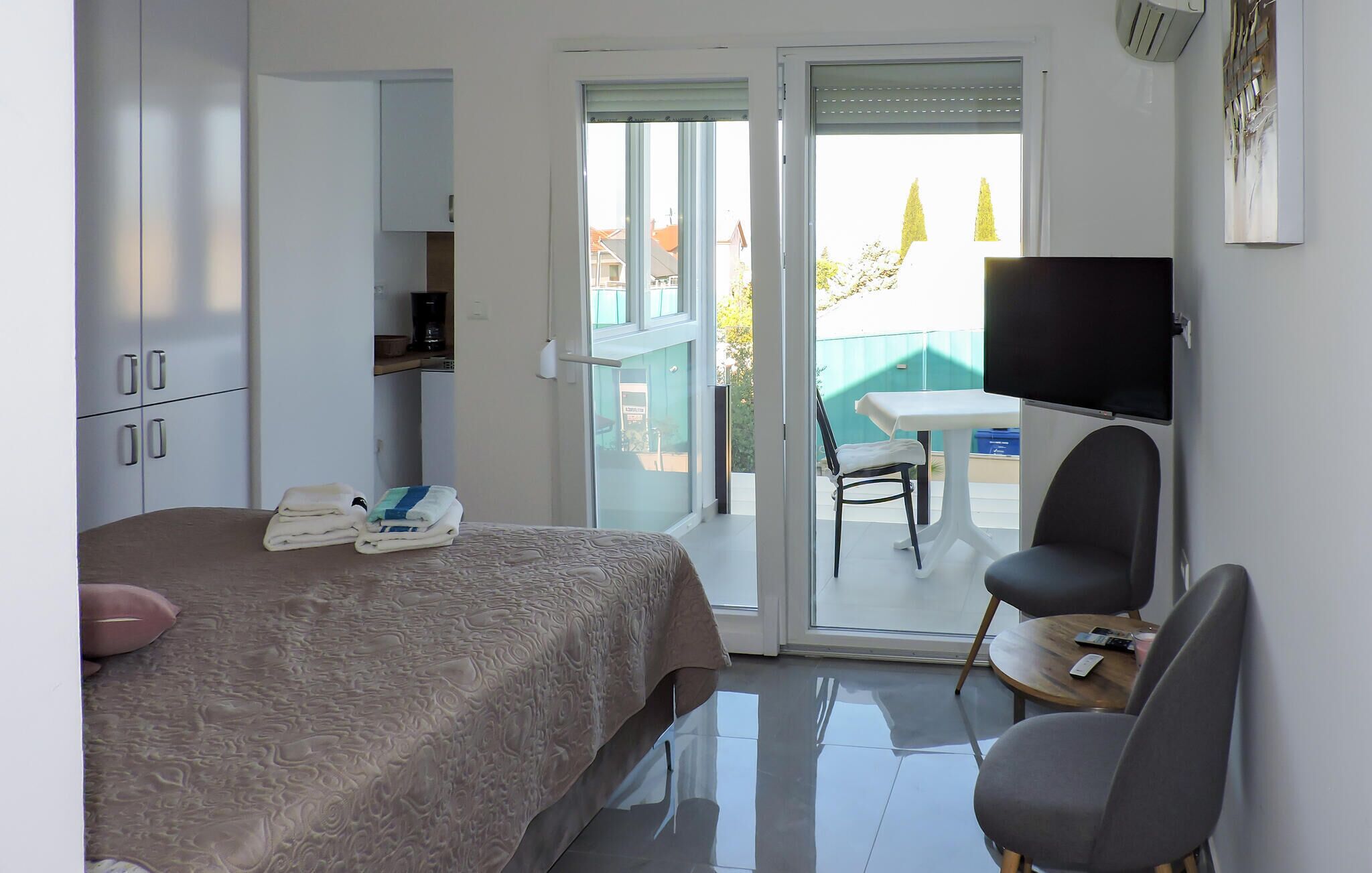 A hotel room with a bed, a desk, a chair, a television, and a balcony with a table and chairs.