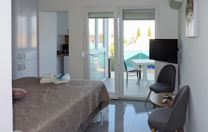 A hotel room with a bed, a desk, a chair, a television, and a balcony with a table and chairs. - Nice apartment in Peroj with WiFi (Peroj)