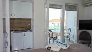 Ett hotellrum med en säng, ett skrivbord, en stol, en TV, ett litet kök och en skjutdörr i glas som leder ut till utsidan.