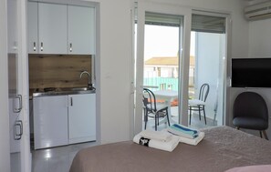 Ein Hotelzimmer mit Bett, Schreibtisch, Stuhl, Fernseher, Küchenzeile und einer Schiebeglastür nach draußen.