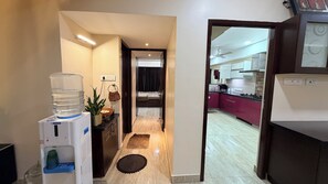 Corredor que dá para um quarto, com um dispensador de água, uma planta e um pequeno tapete.