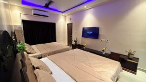 Quarto com duas camas, televisão de tela plana na parede, aparelho de ar condicionado e ventilador de teto.