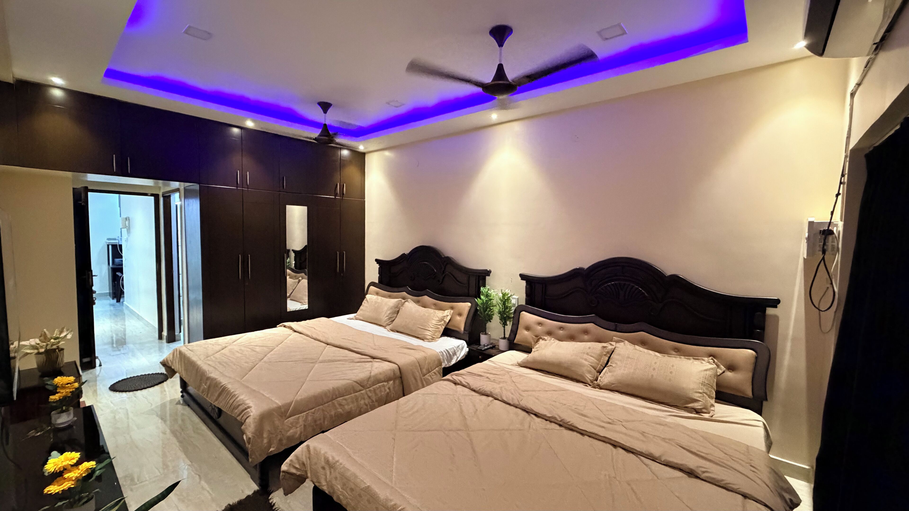 A bedroom with two beds, dark wood wardrobes, a ceiling fan, and a small potted plant.