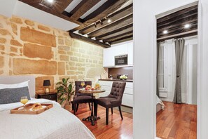 A bedroom with a stone wall, a bed with a tray of breakfast, a chair, and a table with fruit and juice. - Cosy Studio Near Louvre & Les Halles (Paris)