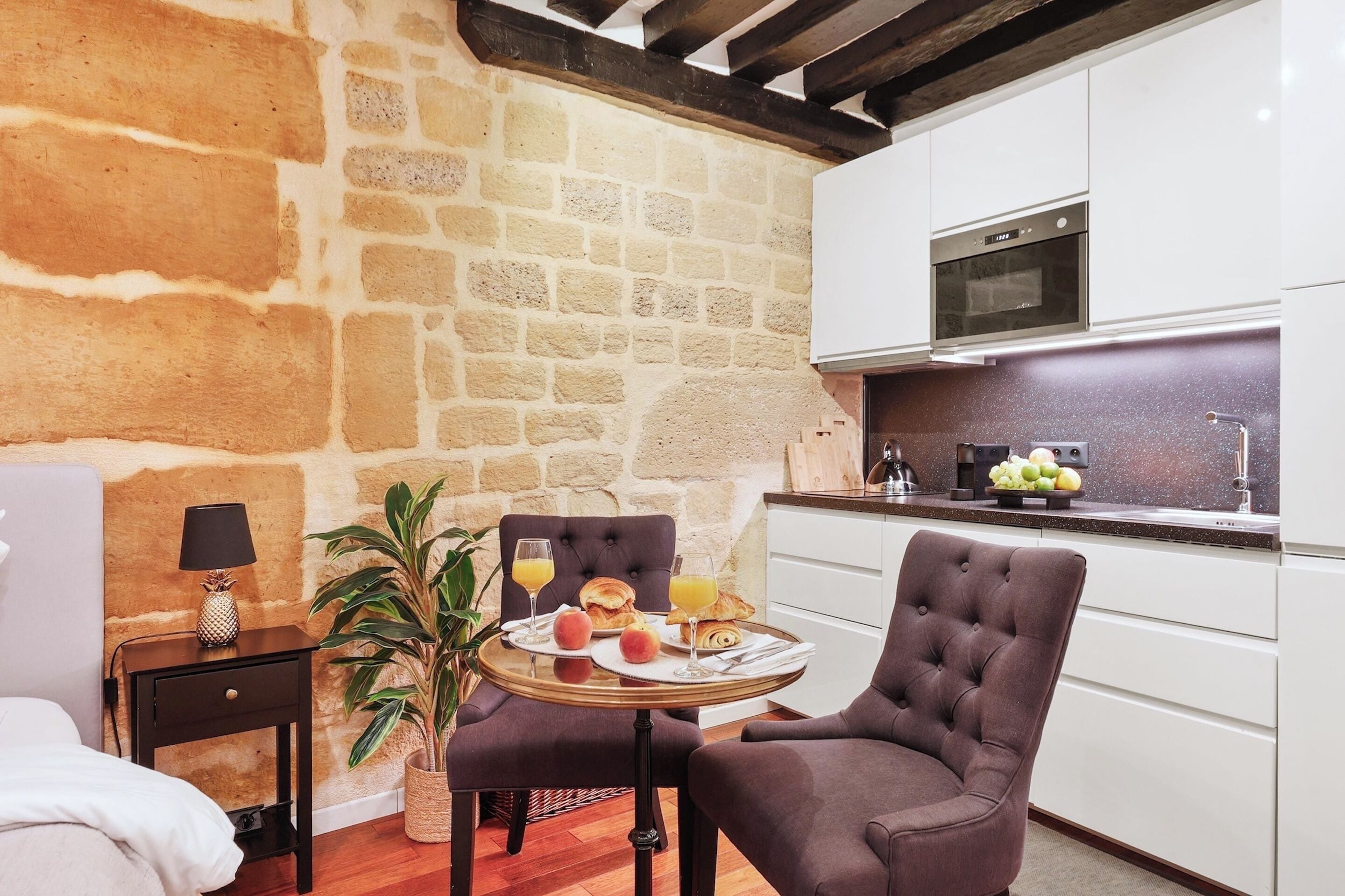 Una habitación acogedora con pared de piedra, cama, una pequeña mesa con desayuno, una silla y kitchenette.