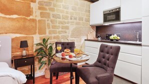 Una habitación acogedora con pared de piedra, cama, una pequeña mesa con desayuno, una silla y kitchenette.