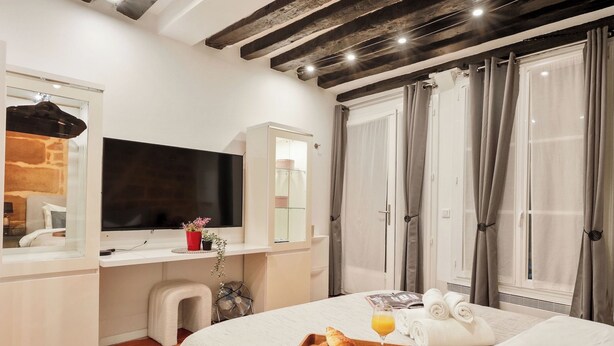 Habitación de hotel con cama, televisor, escritorio con espejo, ventana con cortinas y bandeja de desayuno sobre la cama.