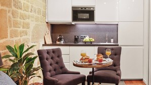 Cocina compacta con armarios blancos, horno integrado y encimera de granito. Un pequeño comedor con dos sillas y una mesa dispuesta con comida y bebidas.