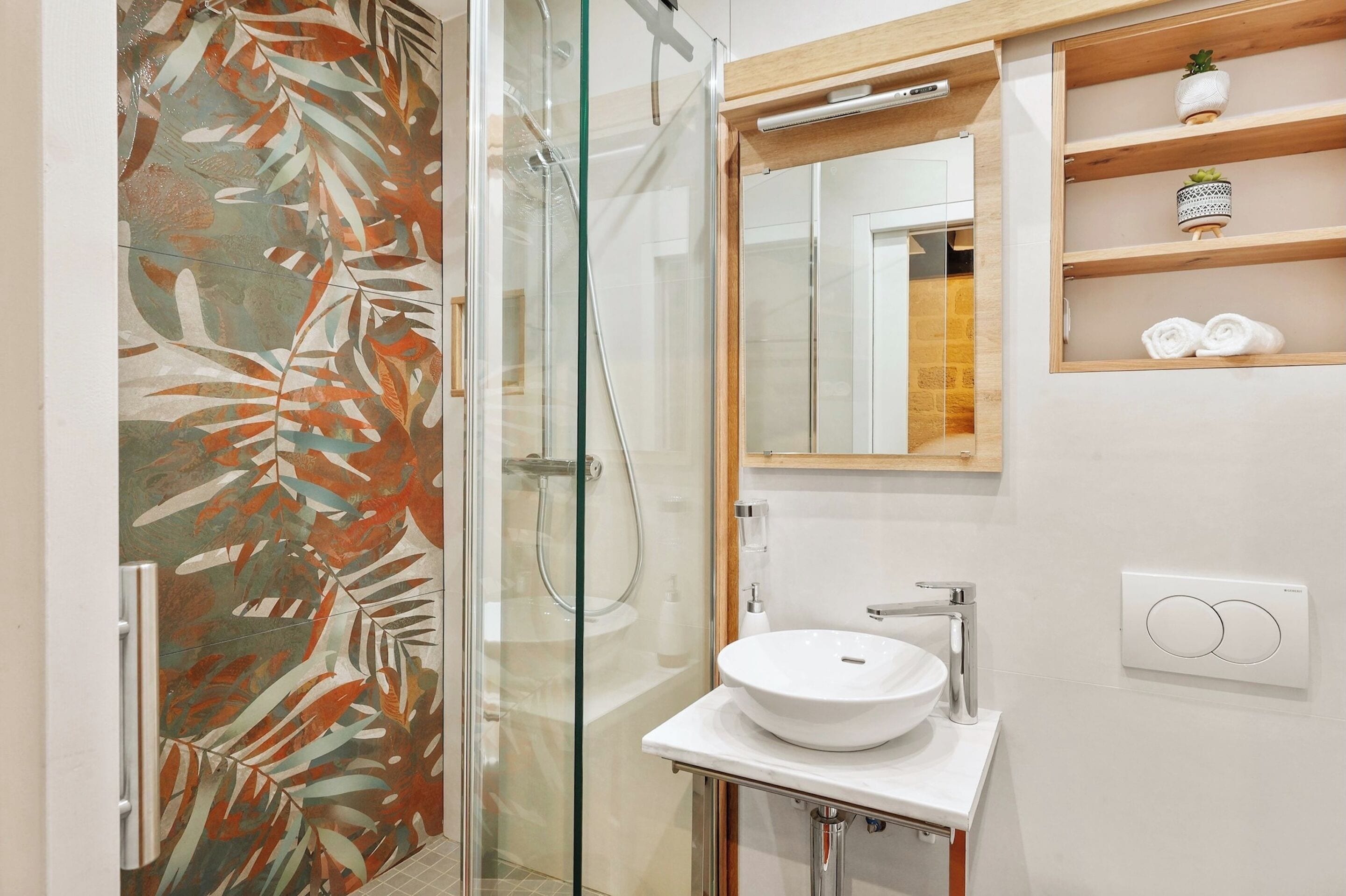 A bathroom with a glass shower enclosure, a white sink, a mirror, and a shelf with towels.
