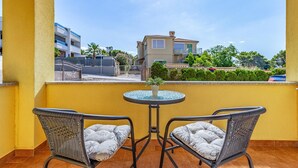 En balkon med to fletstole og et lille bord, med udsigt over et boligområde med bygninger og grønt.