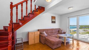 Ein Wohnzimmer mit einer Holztreppe, einer Couch, einem kleinen Tisch und Meerblick durch große Fenster.