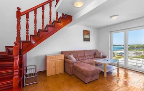 Ein Wohnzimmer mit einer Holztreppe, einer Couch, einem kleinen Tisch und Meerblick durch große Fenster.