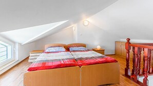 Ein Schlafzimmer mit schrägen Wänden, einem Bett mit karierter Bettdecke, einem Nachttisch mit Lampe und einem Holzschrank.