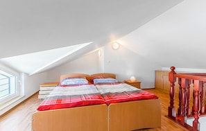 Ein Schlafzimmer mit schrägen Wänden, einem Bett mit karierter Bettdecke, einem Nachttisch mit Lampe und einem Holzschrank.
