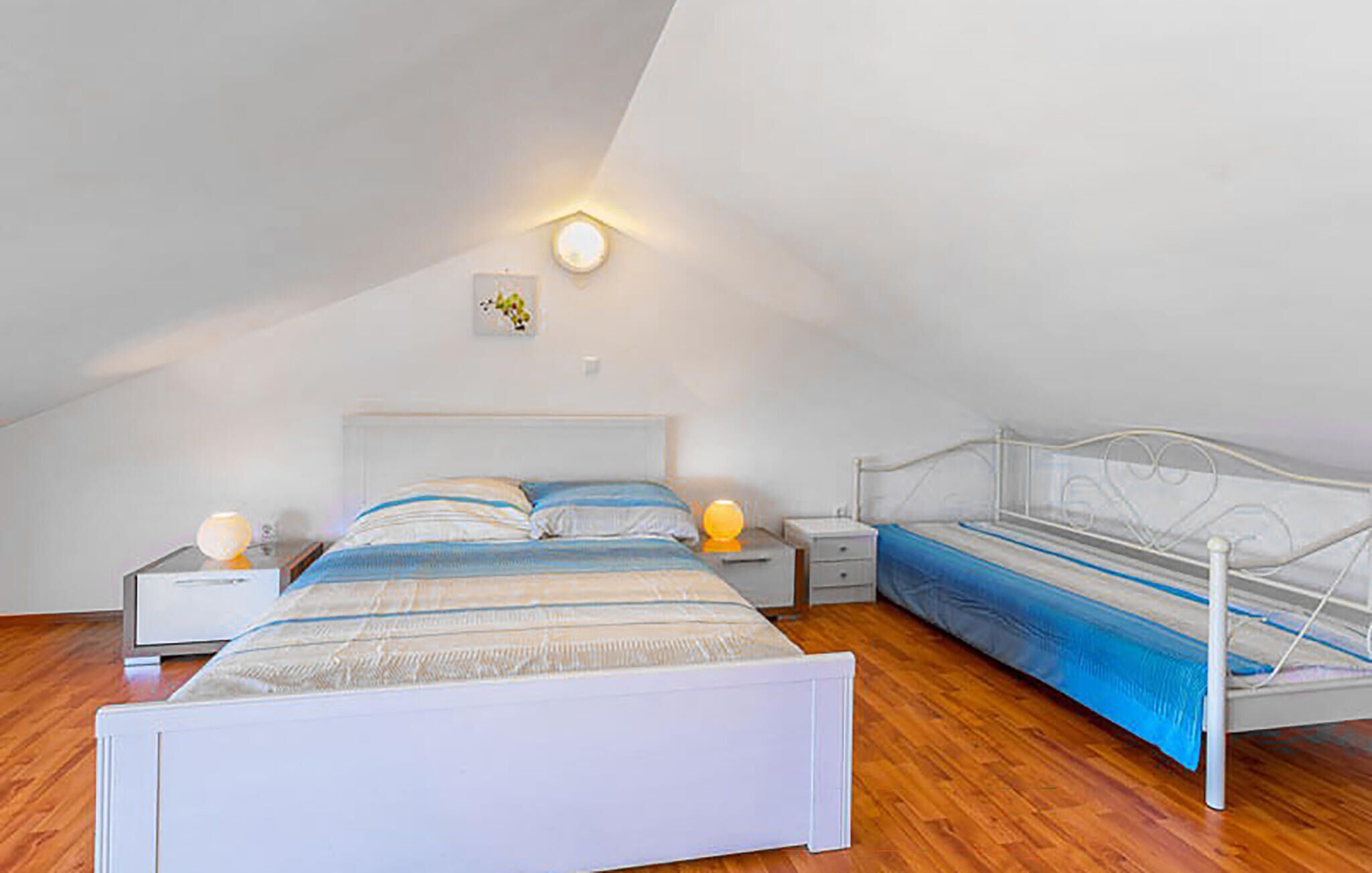 A bedroom with a sloped ceiling, a bed with a white frame, a bedside table with a lamp, and a wall-mounted light fixture.