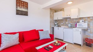 A compact living space with a red sofa, a small dining table, and a kitchenette with white cabinets and a microwave. - Apartment in Medulin (758) (Medulin)