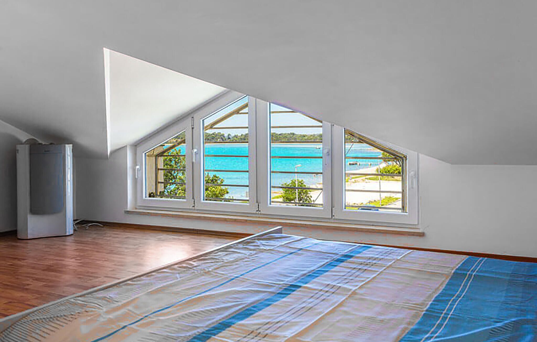 A room with a sloped ceiling, a large window with multiple panes, and a wooden floor.