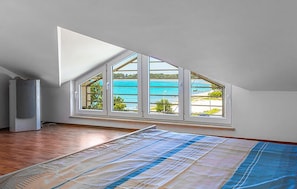 Ein Zimmer mit schrägem Dach, einem großen Fenster mit vielen Sprossen und Holzboden.