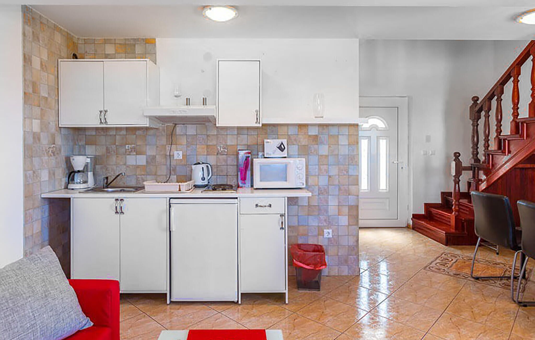 A compact kitchen with white cabinets, a microwave, a coffee maker, and a trash bin.