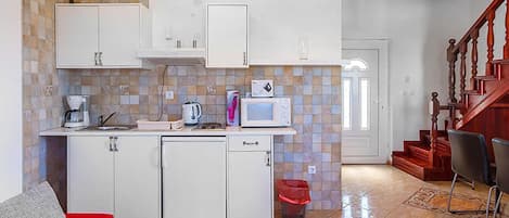 A compact kitchen with white cabinets, a microwave, a coffee maker, and a trash bin.