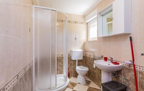 Ein Badezimmer mit Duschkabine, Toilette, Waschbecken und einem an der Wand angelehnten Mop.