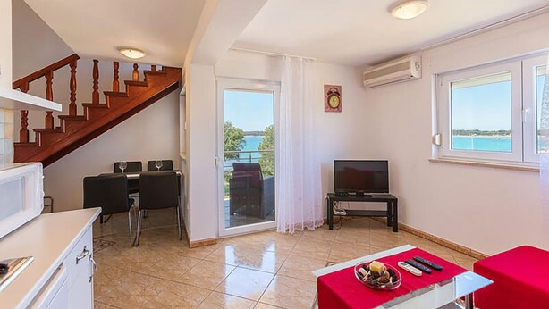 A living room with a TV, a dining area with chairs, a staircase, and a view of the outdoors. - Apartment in Medulin (758) (Medulin)