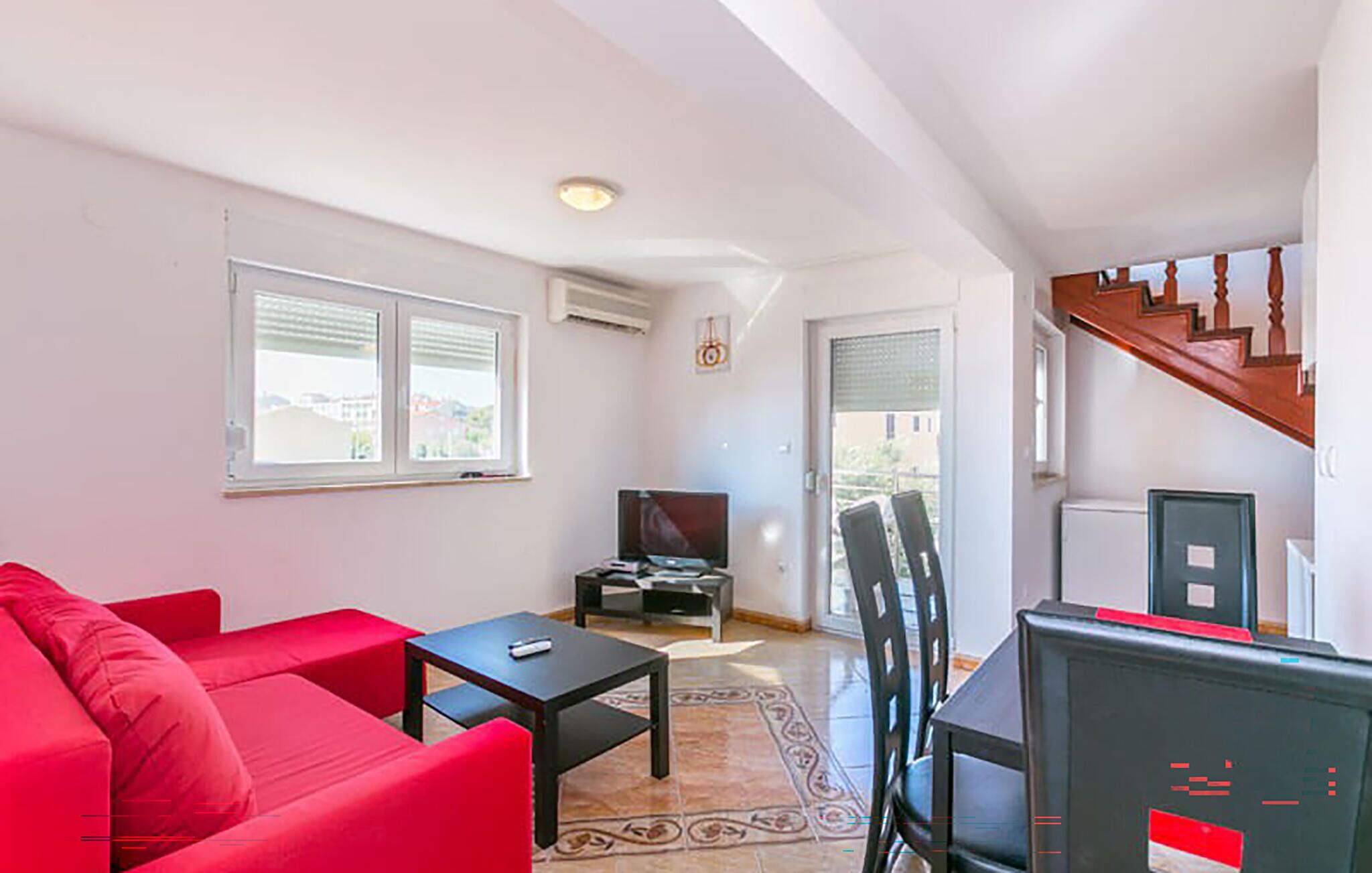 A living room with a red sofa, a black table, and a TV. There is a staircase leading to another level.