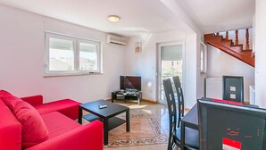 A living room with a red sofa, a black table, and a TV. There is a staircase leading to another level. - Apartment in Medulin (760) (Medulin)