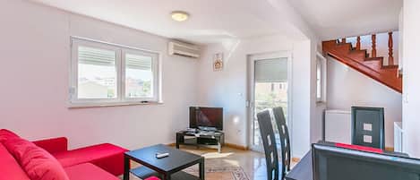 Un salon avec un canapé rouge, une table noire et un téléviseur. Un escalier mène à un autre niveau.