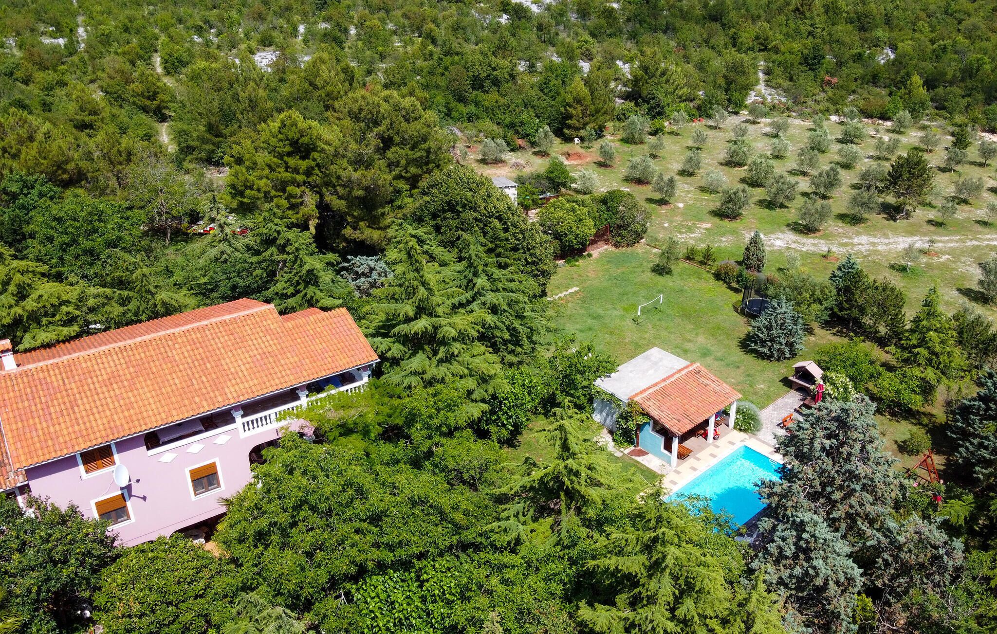 Une grande maison avec une piscine, entourée d’une végétation luxuriante et d’arbres.
