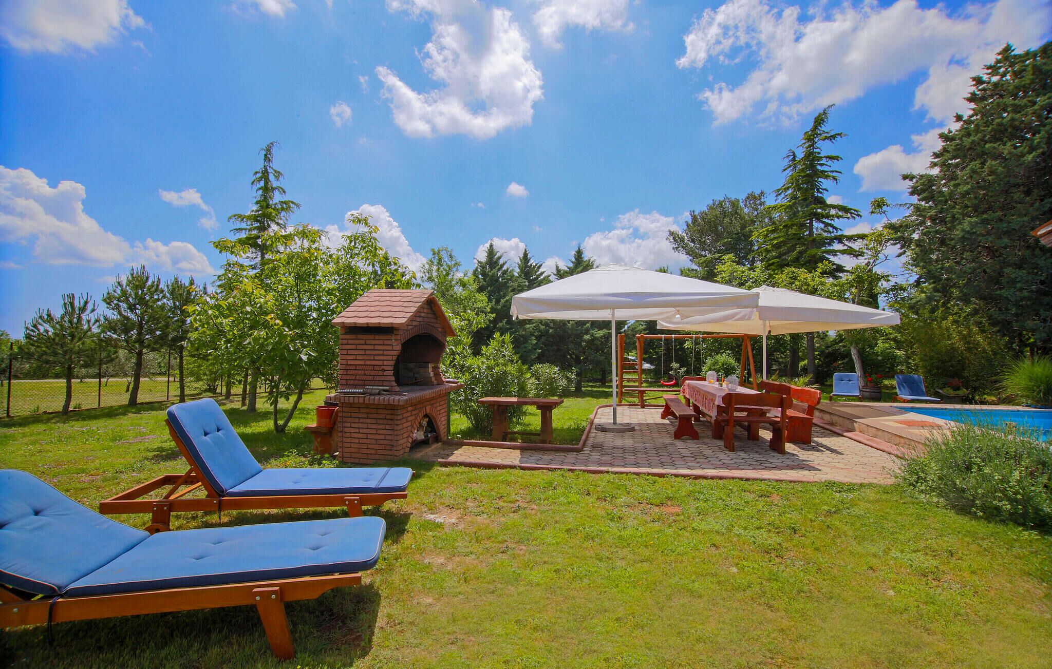 Un jardin avec un barbecue, des chaises longues, une table avec un parasol et une piscine.