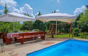 Ein Poolbereich mit einer Holzbank, einem Picknicktisch und zwei Sonnenschirmen, die Schatten spenden.