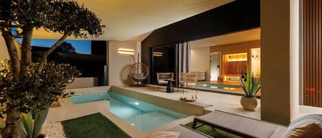 Un área de piscina moderna al aire libre, con mobiliario y un gran árbol.