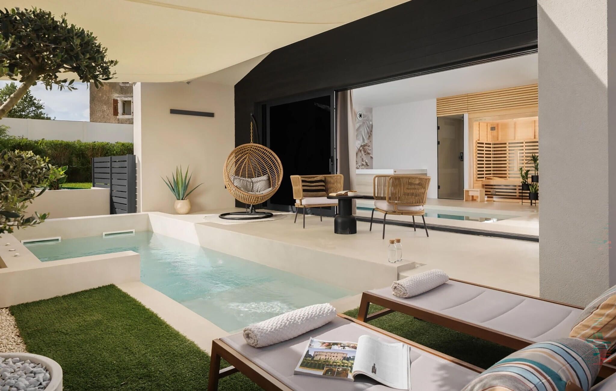 Un espace piscine extérieur moderne, doté de chaises longues, d’un fauteuil suspendu et d’une petite table avec un magazine.