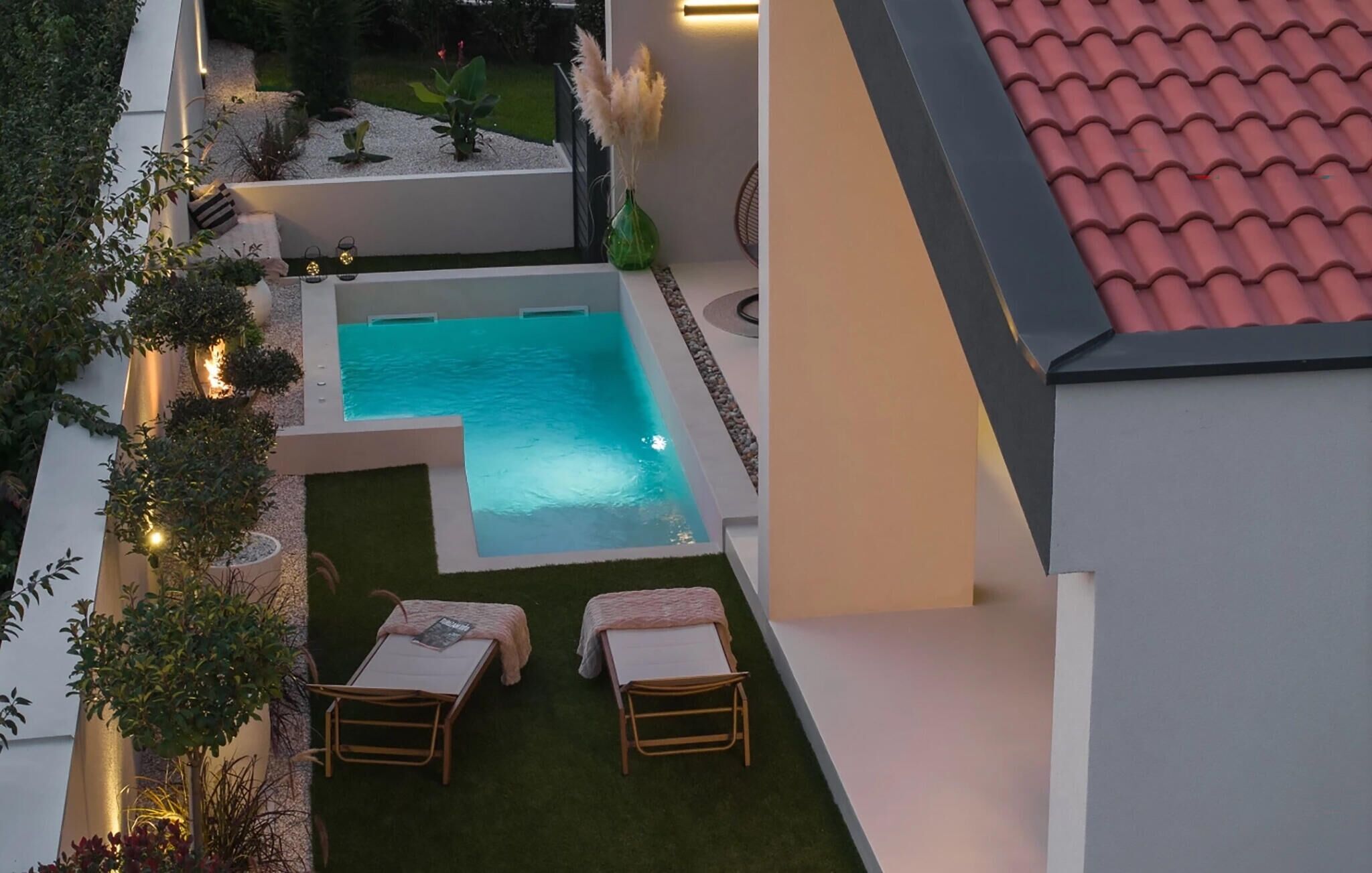Una piscina en la azotea con dos tumbonas, rodeada de vegetación y un pequeño jardín.
