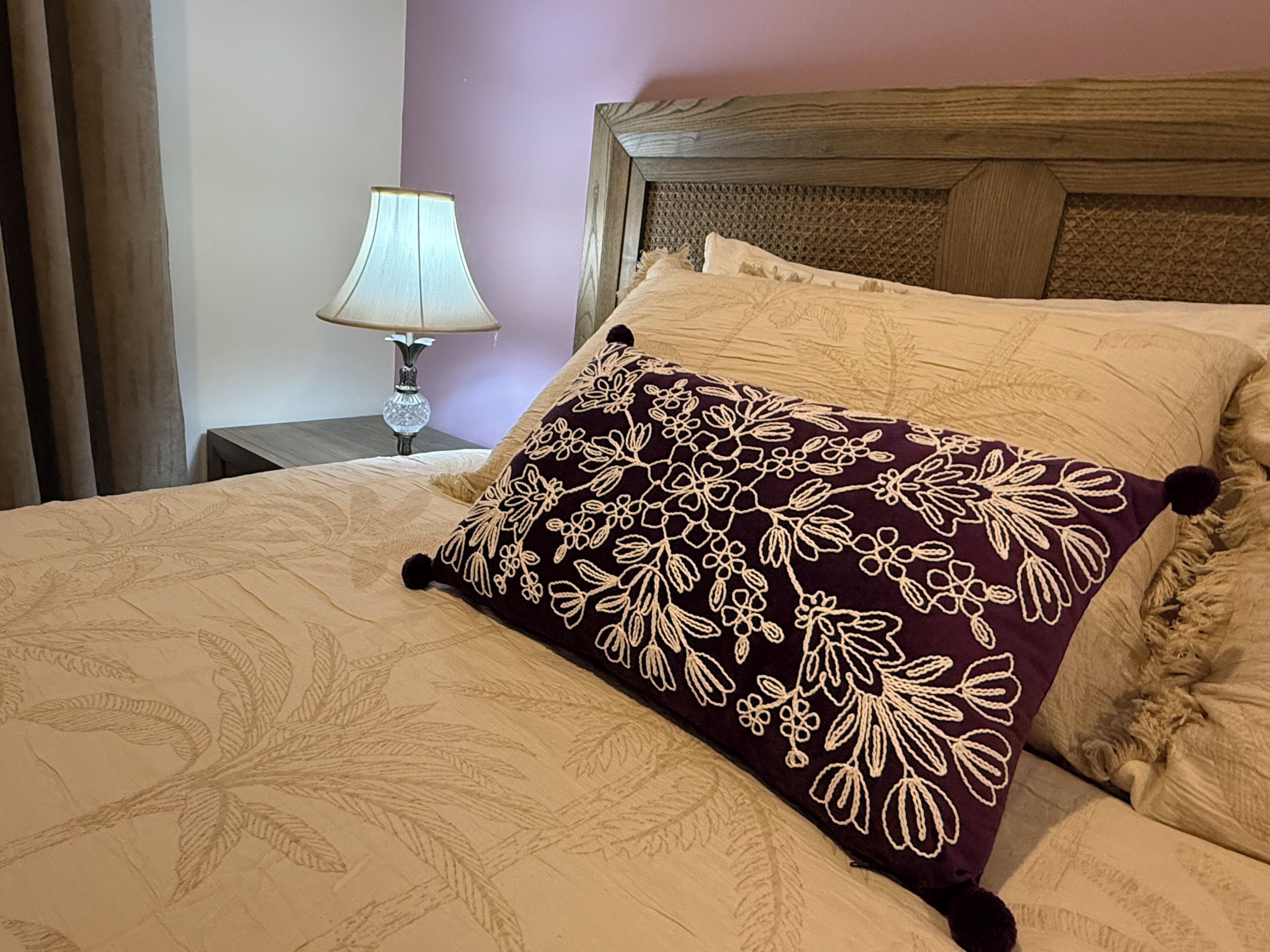 A bed with a floral patterned pillow, a wooden headboard, and a nightstand with a lamp.