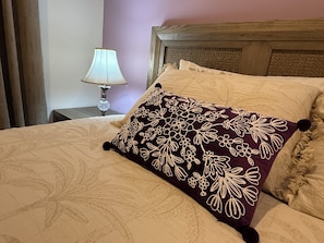 Ein Bett mit einem blumigen Kopfkissen, einem Holzkopfschild und einem Nachttisch mit einer Lampe.