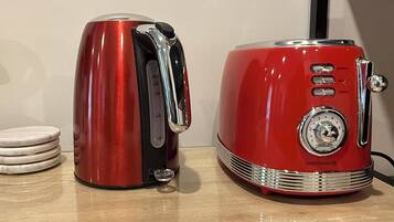Two red appliances, a kettle and a toaster, on a wooden surface with stacked coasters.