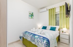 Een slaapkamer met een bed, nachtkastje, lamp, airconditioning en een raam met gordijnen.