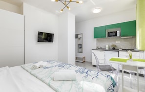 Ein modernes Hotelzimmer mit Bett, Fernseher, Küchenzeile und Badezimmer.