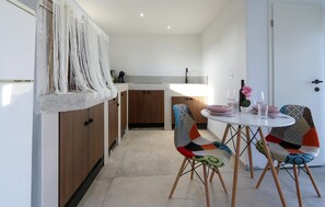 Een moderne keuken met houten kastjes, een wit aanrechtblad en een eethoek met een ronde tafel en kleurrijke stoelen.