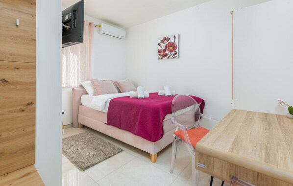 Ein Schlafzimmer mit Bett, Nachttisch, Sessel, Fernseher und Klimaanlage.