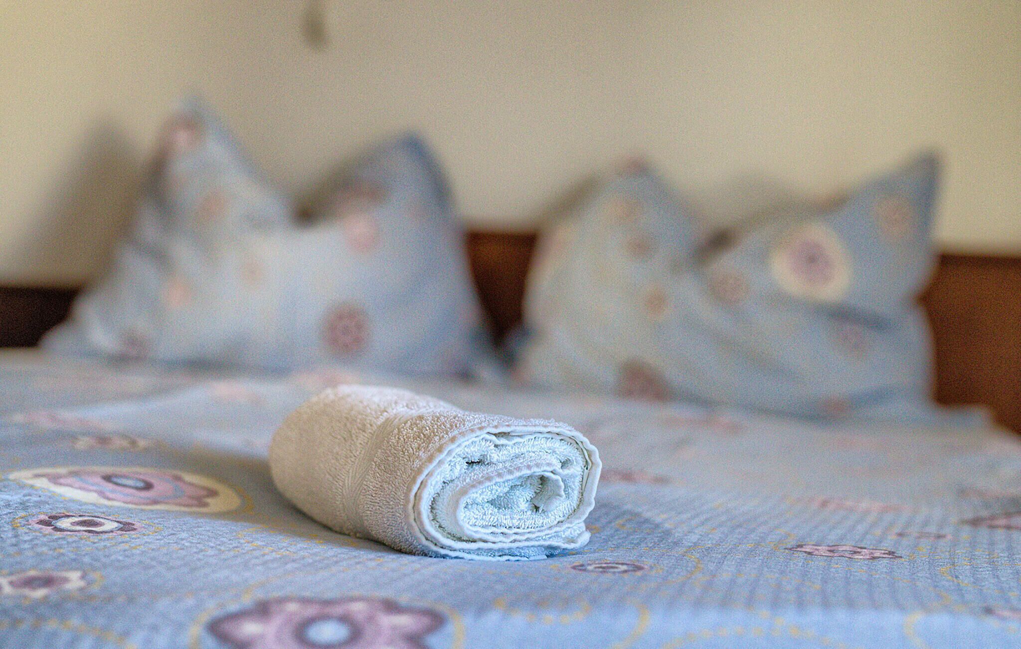 A neatly made bed with a rolled towel, a patterned bedspread, and several pillows with floral designs.
