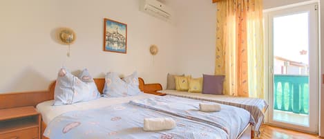 A hotel room with a large bed, a smaller bed, a wooden nightstand, a dresser, a painting on the wall, an air conditioning unit, and a view of a balcony with a railing.