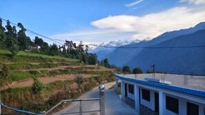 Un edificio con techo azul y paredes blancas, situado en una ladera con campos en terrazas y montañas al fondo.