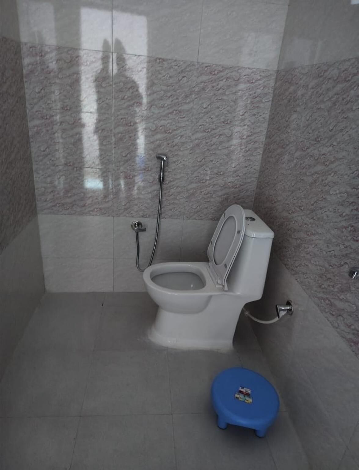 Baño con inodoro, ducha y un taburete azul.