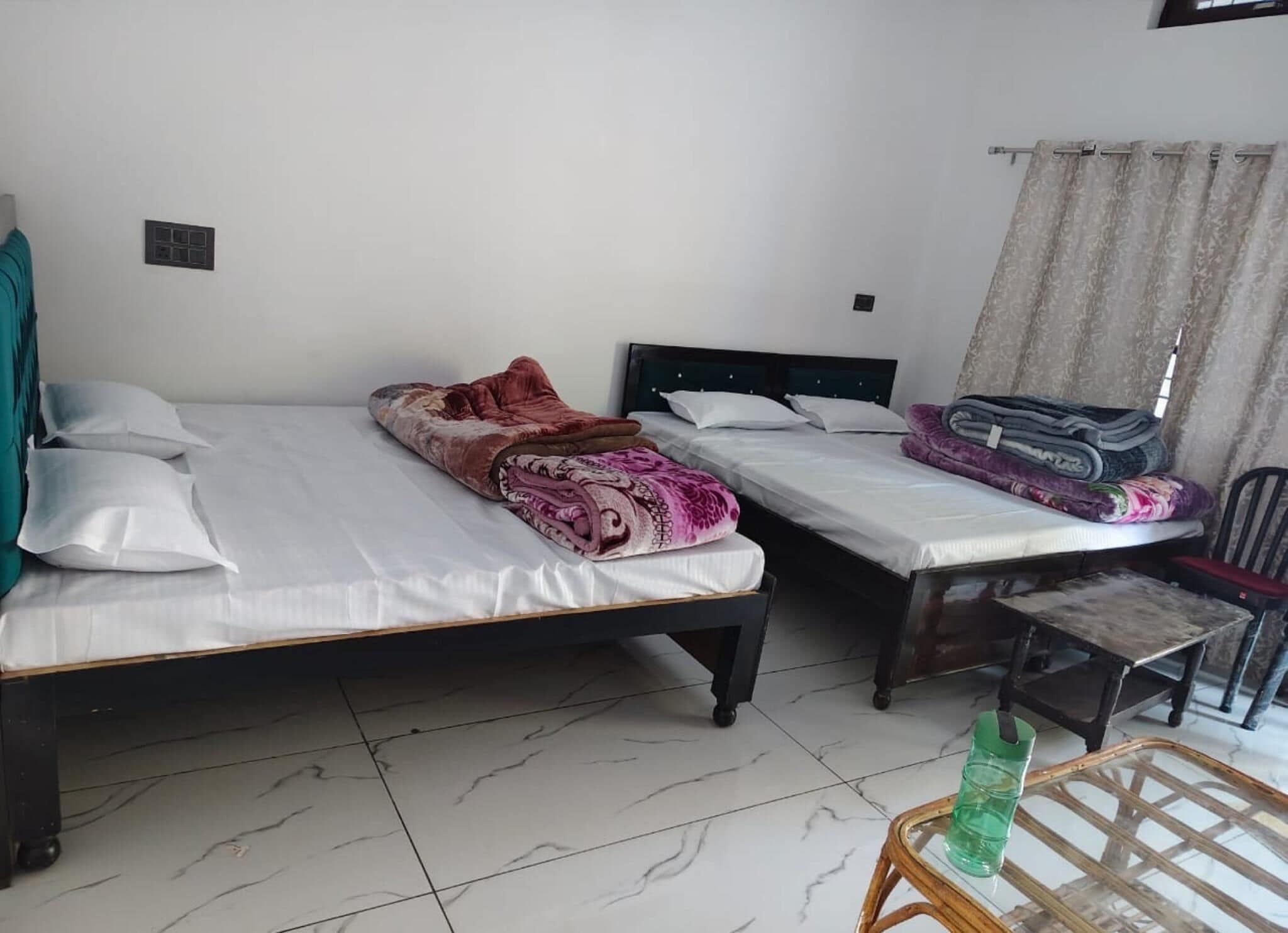 Una habitación con dos camas individuales, una mesita con una botella y una silla.