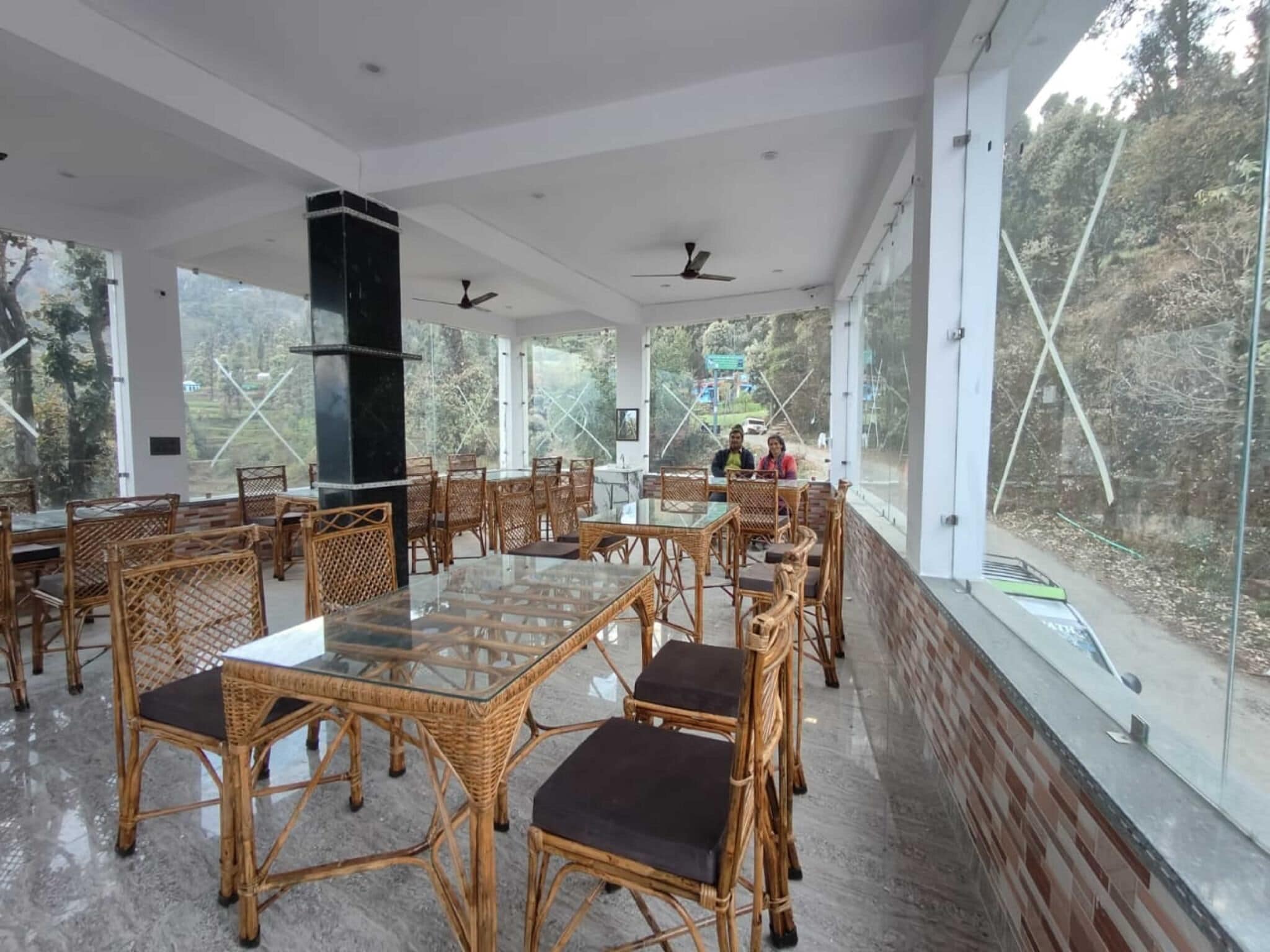 Amplio espacio interior con mesas de vidrio y sillas de mimbre, grandes ventanales con vistas al exterior.