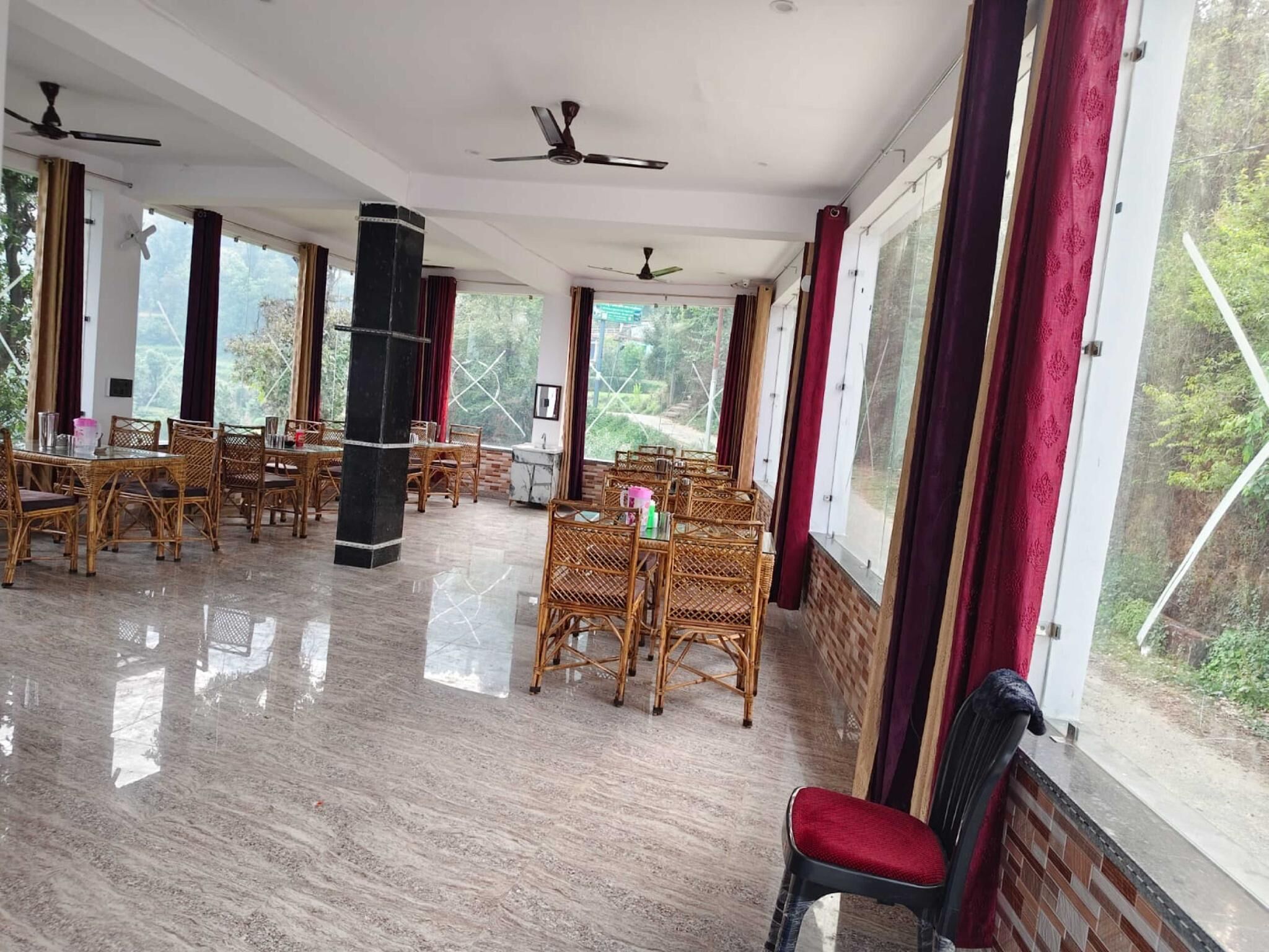 Amplia habitación con varias mesas y sillas, ventanas grandes con cortinas y ventiladores de techo.