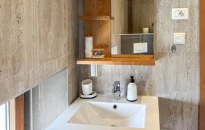 Ein Badezimmer mit einem weißen Waschbecken, einem Spiegel, einem Holzregal mit Toilettenartikeln und einem Handtuchhalter.